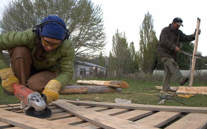 Two people use tools to work on pieces of wood during a service project with outward bound. 